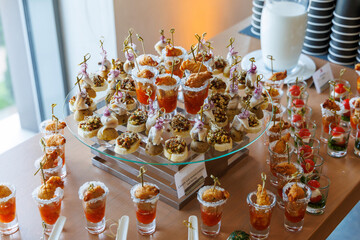 Appetizers served in shot glasses and on skewers, arranged on a tiered tray and buffet table