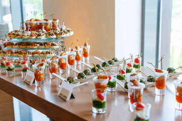 Elegant buffet table with layered appetizers in glass cups, skewered bites on white plates, and tiered hors d’oeuvres