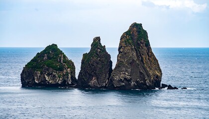 Naklejka premium Three Jagged Volcanic Rock Formations Rising from Calm Blue Ocean
