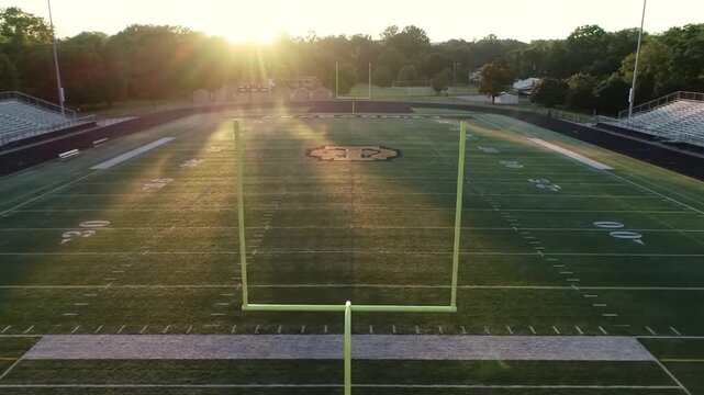 An empty American football field at sunrise, with a dramatic lens flare creating a hopeful or nostalgic atmosphere.