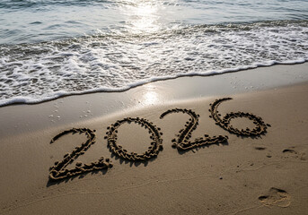 The year 2026 written in the sand on a beach with gentle ocean waves washing ashore under the bright sunlight