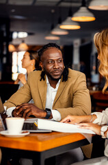 Obraz premium Businessman and female coworker talking about work while using laptop in modern coffee shop.