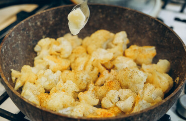 A close-up of sautéed cauliflower in a rustic pan, seasoned and cooking on a stove.