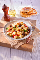 Nudelsalat mit Oliven und Zucchini auf grauem Steingutteller auf gedecktem Tisch, fetakäse, tellergericht, 