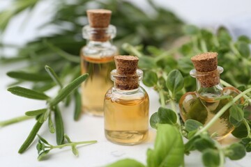 Bottles of essential oil and herbs on white marble table, closeup