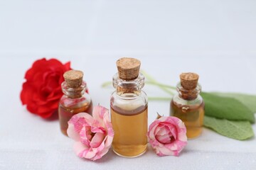 Bottles of cosmetic products, roses and sage on white table, closeup