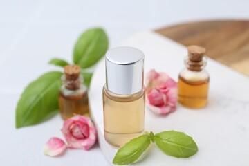 Bottles of cosmetic products, roses and basil on white table, closeup
