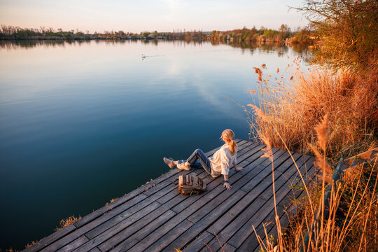 Tranquil lake scenery with woman relaxing on pier while swan swimming in distance. Connection and harmony with nature. Mindfulness moment - Powered by Adobe