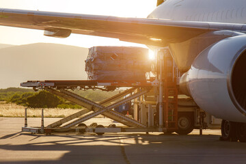 Cargo being loaded into a commercial airplane during sunset at an airport runway
