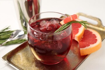 Tasty cocktail with grapefruit, ice cubes and rosemary on white table, closeup