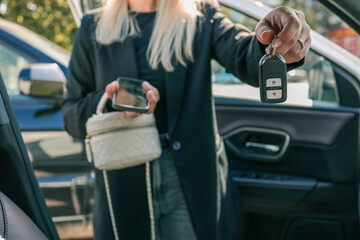 Woman holding car key fob while standing near vehicle, close-up of hand with modern remote control and blurred background of automobile