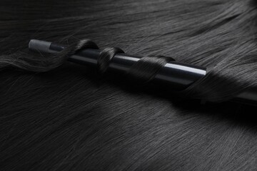 Naklejka premium Curling iron with shiny black hair, closeup
