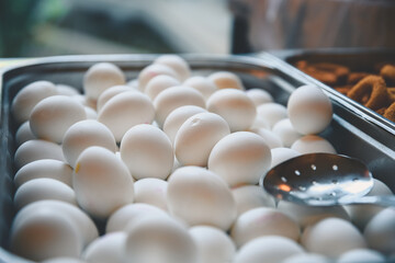 Piled high in a metal serving tray, white eggs await breakfast or brunch, complemented by a metal slotted spoon resting conveniently on top, ready for serving
