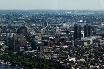 Fototapeta premium Enjoy aerial view of Boston showcasing modern skyscrapers alongside historic buildings, with Zakim Bunker Hill Bridge and Charles River flowing through lush urban environment. Cityscape includes