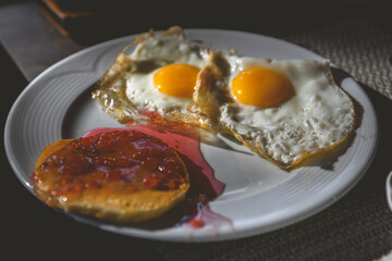 Two perfectly fried eggs and a fluffy pancake topped with vibrant raspberry jam rest on a pristine white plate, creating a delightful and energizing breakfast scene