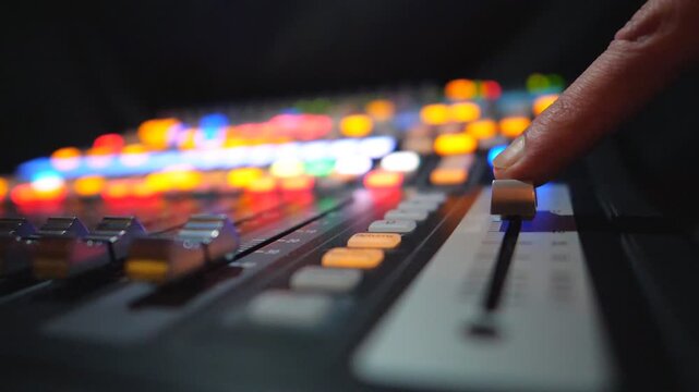 Finger of male dj moving button on soundboard. Blurred background with brightly glow keys. Modern sound equipment in recording studio. Musical player at party in night club. Slow motion Close up