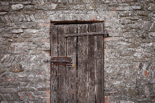 Vecchia porta in legno con chiavistello e lucchetto su un muro in pietra e mattoni