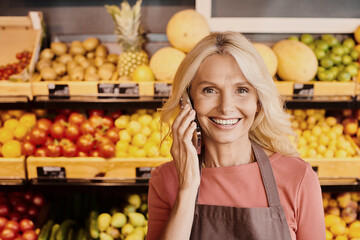 Smiling blonde saleswoman assists customers at a vibrant organic farmers market store