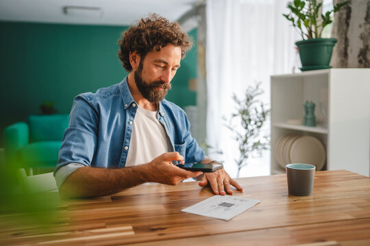 Freelancer scanning qr code on invoice with smart phone at home