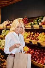 Blonde woman selects fresh organic produce in a cozy farmers market grocery store