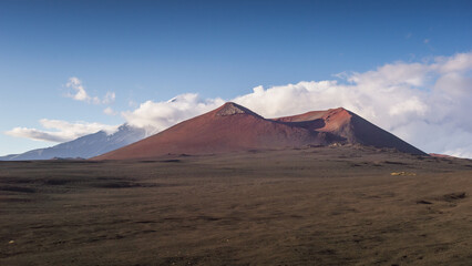 Majestic volcanic landscape featuring two distinct mountains with reddish slopes, surrounded by a vast barren terrain under a clear blue sky, showcasing natural beauty and geological formations