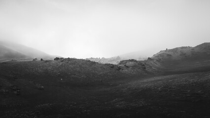 Black and white landscape of rugged terrain with misty atmosphere, showcasing dramatic hills and...