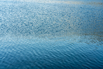 Textured water surface with gentle ripples reflecting light and color variations in a natural abstract pattern