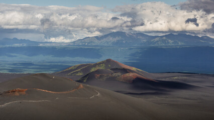 Majestic volcanic landscape featuring black sand dunes, colorful volcanic cones, and distant mountains under a dramatic sky, showcasing the beauty of nature's geological formations