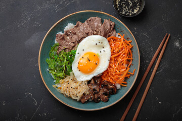 Bibimbap, authentic korean dish with a steamed rice topped with fried egg, beef, colorful vegetables, traditional dish of Korea top view on black background