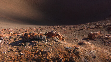 Rocky terrain with volcanic soil and scattered boulders, showcasing the unique geological features of a barren landscape under a clear blue sky, emphasizing natural beauty and ruggedness