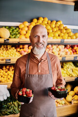 Salesman showcasing fresh organic strawberries in a vibrant grocery store