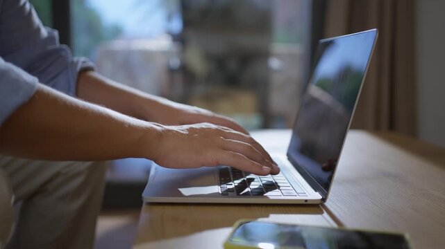 Close up view of caucasian millennial man hands typing on a laptop keyboard while sitting at home, symbolizing remote work, freelance productivity, and digital technology.