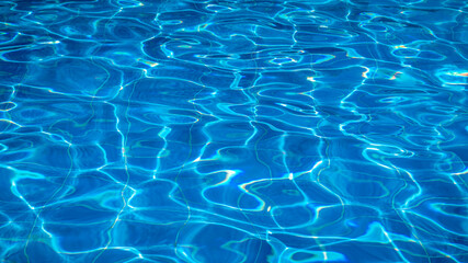 Sunlight reflecting on the rippling water surface of a swimming pool creates a beautiful and mesmerizing pattern of light and shadow, perfect for backgrounds and summer-themed projects