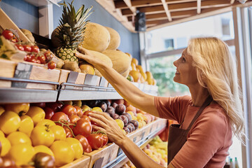 Blonde saleswoman curates fresh organic produce in a vibrant grocery store