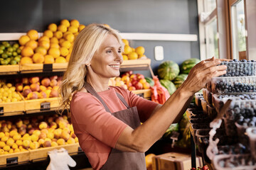 Blonde saleswoman arranging fresh organic blueberries in vibrant farmers market store