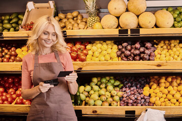 Blonde saleswoman assists customers in vibrant organic produce section of grocery store