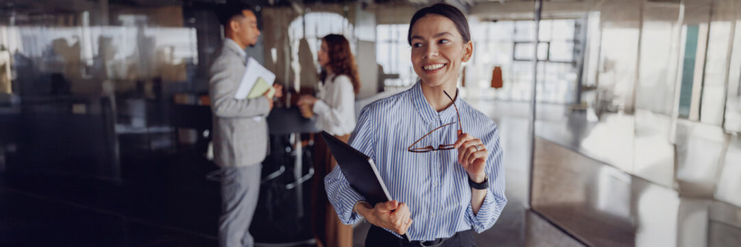 A smiling businesswoman with glasses and a notebook showcases professionalism in a modern workplace - Powered by Adobe