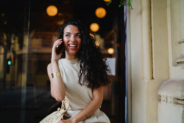 Woman talking on smartphone outside, radiating positivity and confidence, representing flexibility of mobile-first work culture and global communication.