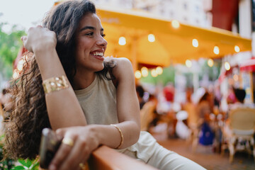 Smiling woman with smartphone turns sideways, reflecting candid joy and real-time connectivity in modern urban life.