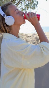 Woman Drinking from Red Can with Headphones Outdoors