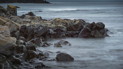 Rocky shoreline with smooth waves gently lapping against the dark stones, creating a serene coastal atmosphere, ideal for nature and landscape photography enthusiasts