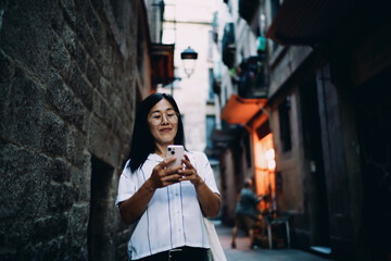 Obraz premium Asian woman checks smartphone in narrow alley, confidently navigating digital life, embodying modern independence, digital flow and tech-first self-awareness.