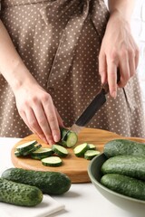 Woman cutting fresh cucumber at white table, closeup