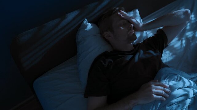 Young man unable to sleep, suffering from insomnia lies awake in bed at night. Sleep disorders, stress anxiety and overthinking. Depression and burnout. Space for text