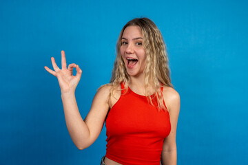 Fototapeta premium Enthusiastic young woman showing ok sign with blue background