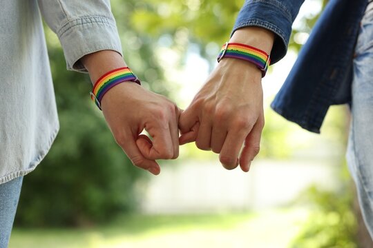 LGBT concept. Women in rainbow wristbands holding hands outdoors, closeup