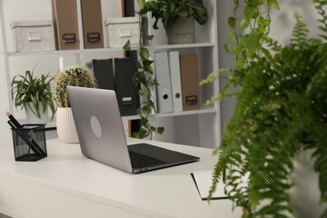 Stylish workplace with laptop, stationery and floral decor in office. Biophilic interior design
