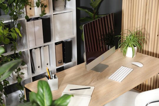 Stylish workplace with modern computer, stationery and floral decor in office. Biophilic interior design