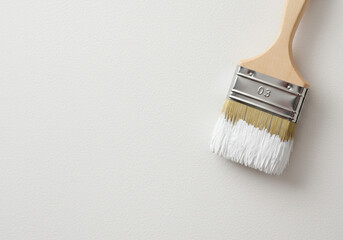 Close up of a paint brush with white paint on the bristles against a white background in a studio shot