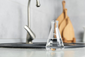 Flask with clean water near sink on counter in kitchen, closeup. Space for text